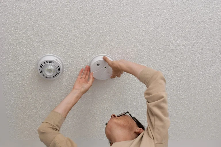 woman hanging carbon monoxide detector on ceiling